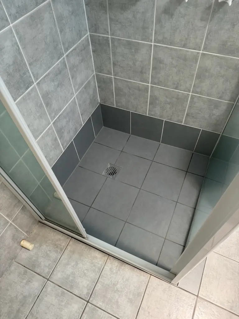 shower base with fresh epoxy grout and new dark accent tiles after professional leak repair